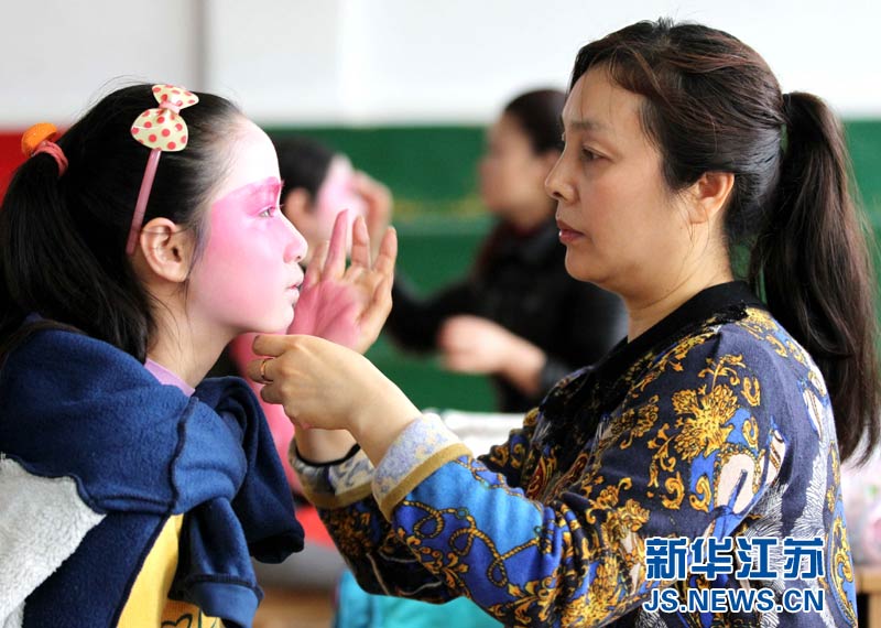 4月17日,江苏省南通市艺术剧院京剧演员为小学员化妆.